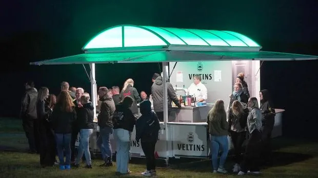 Visitors queueing at a lit drinks stand at night at the Seefest in Großsander